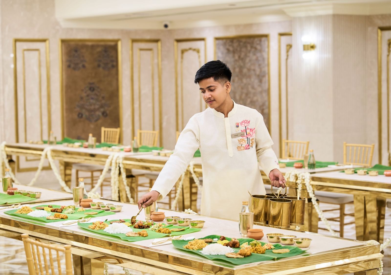A man in a chef's coat arranging food on a beautifully set buffet table within an elegant banquet hall at the Grand Chennai by GRT Hotels.