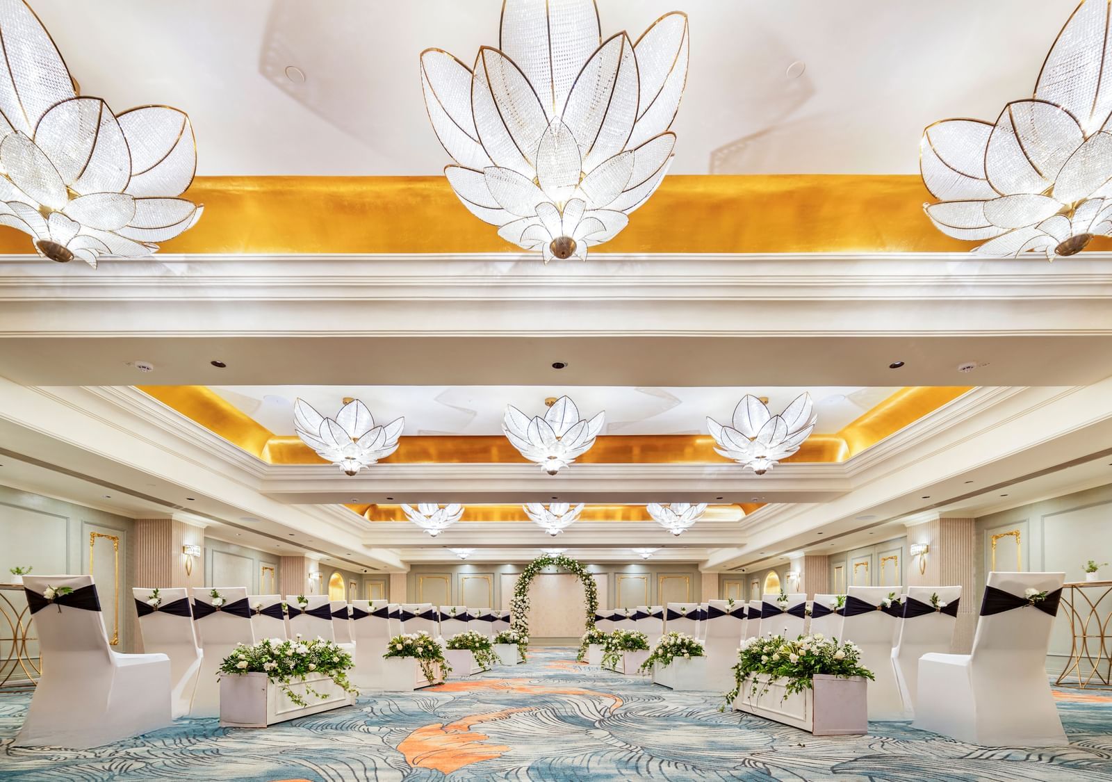 A breathtaking view of an unoccupied, opulent ballroom at Grand Chennai at GRT Hotels, highlighting its soaring ceilings, intricate gold and white decorative elements, and an array of sophisticated, statement-making chandeliers.