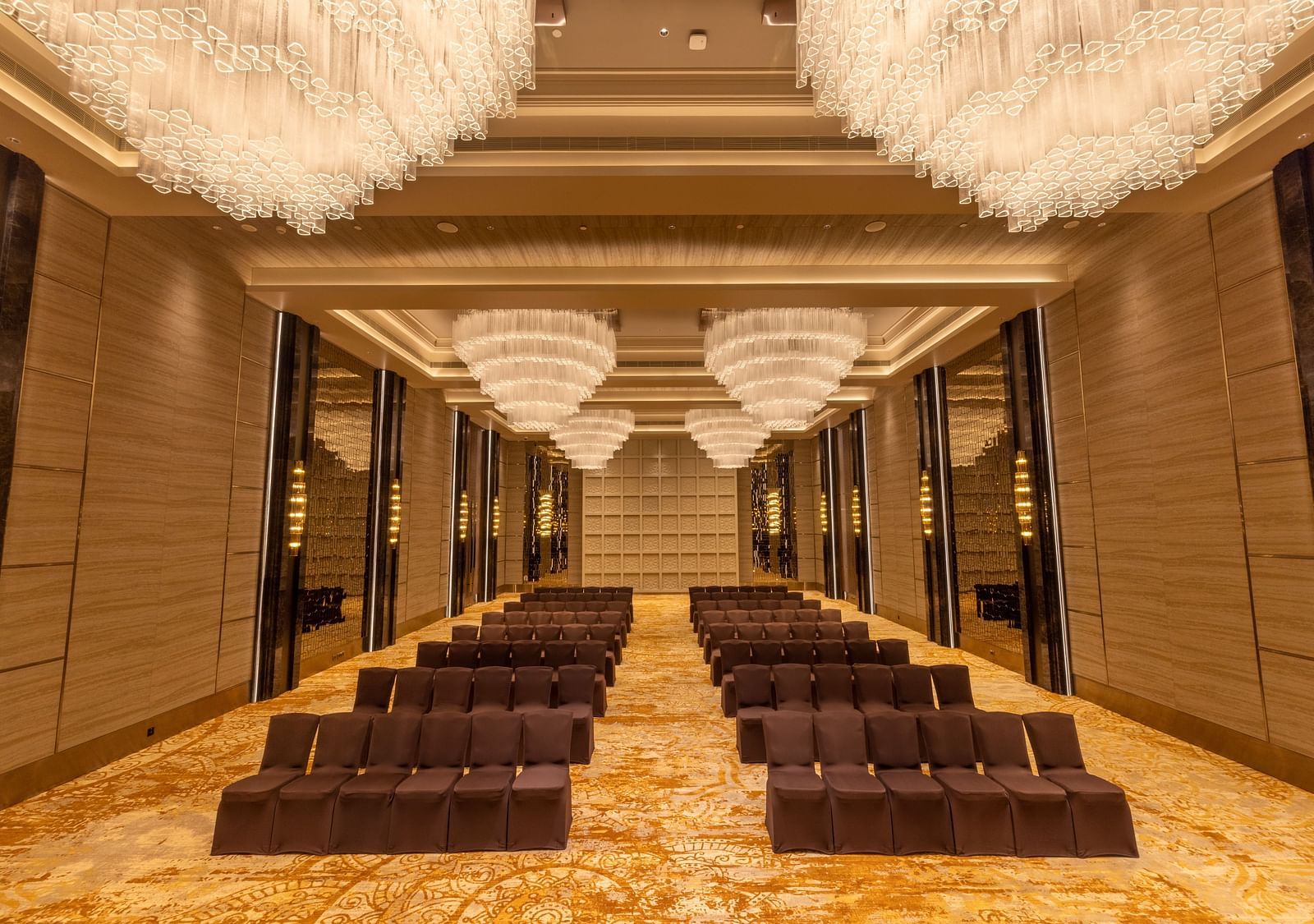 Luxurious banquet hall with rows of chairs and opulent hanging chandeliers. - Grand Madurai by GRT Hotels