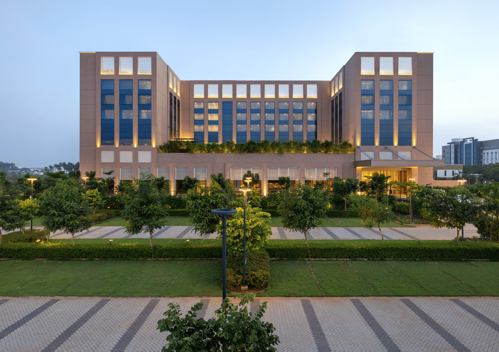 A facade image of our large modern hotel building with numerous windows and manicured landscaping, likely at dusk - Grand Madurai by GRT Hotels