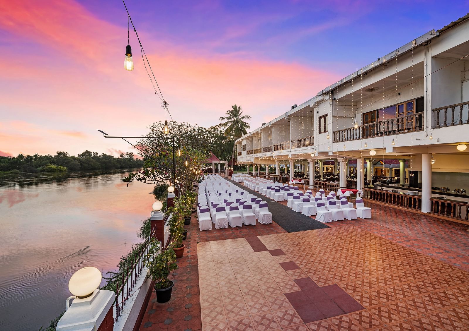 An image of the outdoor event space with seating arrangement near a lake with bright decorative lighting - GReaT Trails River View Resort Thanjavur By GRT Hotels