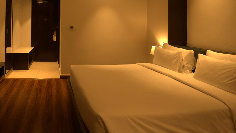 A bedroom at Wedlock Greens Hotels & Resorts, Dhanbad featuring a double size bed, a cabinet table, and a flat TV screen mounted on the wall.