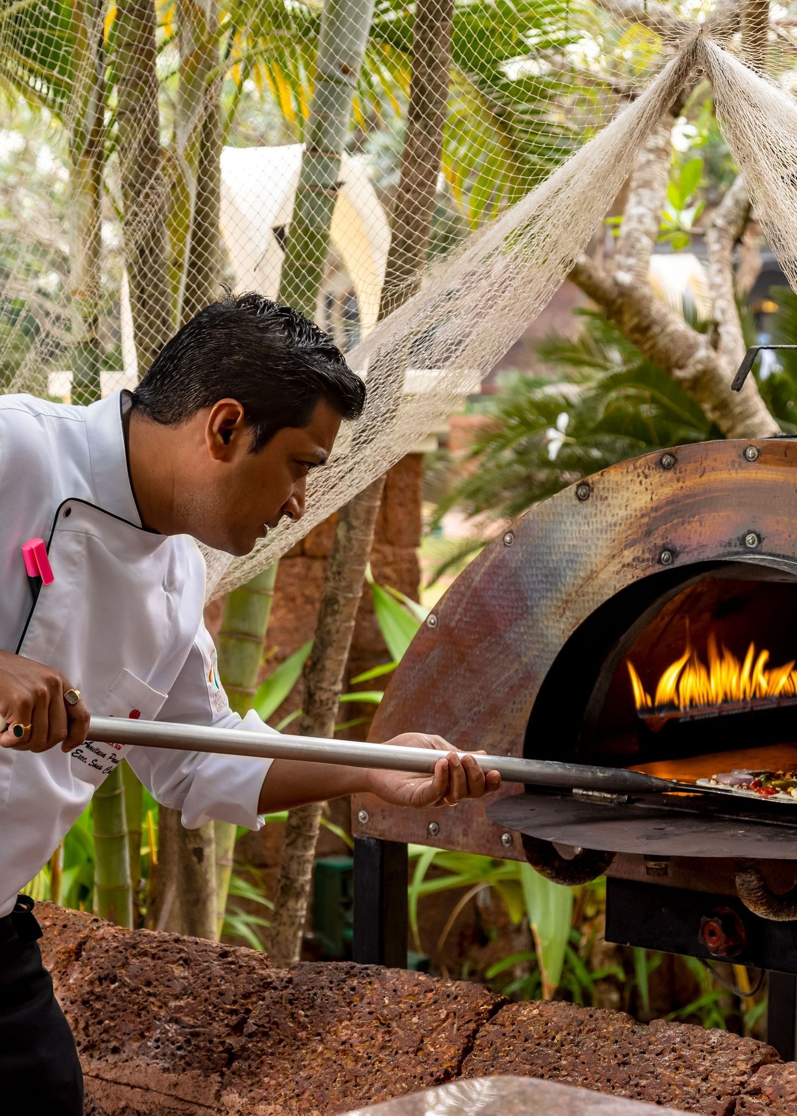 a chef sliding a pizza to cook in a wood-fire oven - Caravela Beach Resort Goa