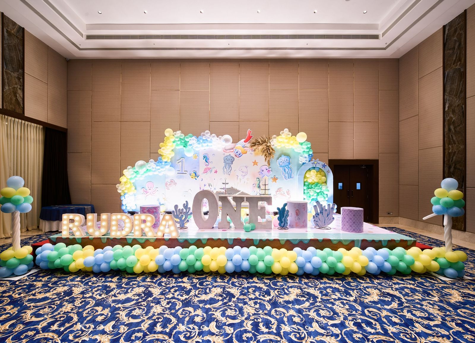 A decoration setting of a stage for a birthday party adorned with balloons and colourful lights at Grand Vijayawada by GRT Hotels