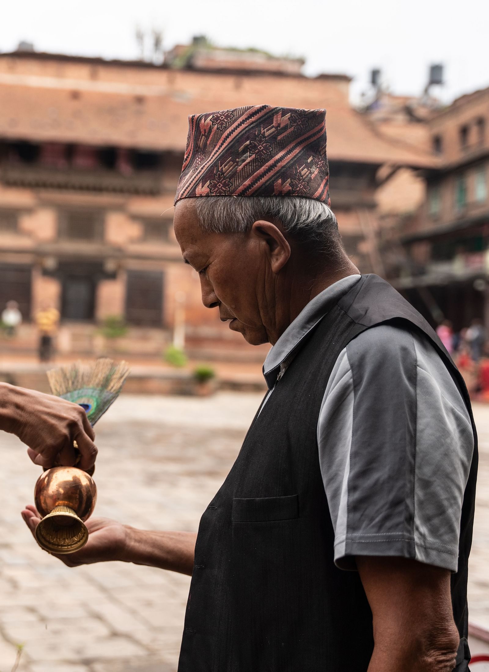 A monk pouring holy water into the palm of an old man