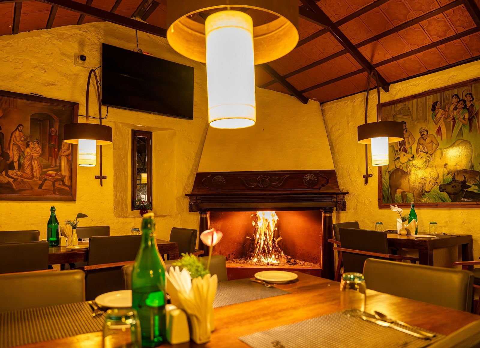 Warmly lit dining area with wooden furniture and decorative wall art. | Mango Hill, Yercaud