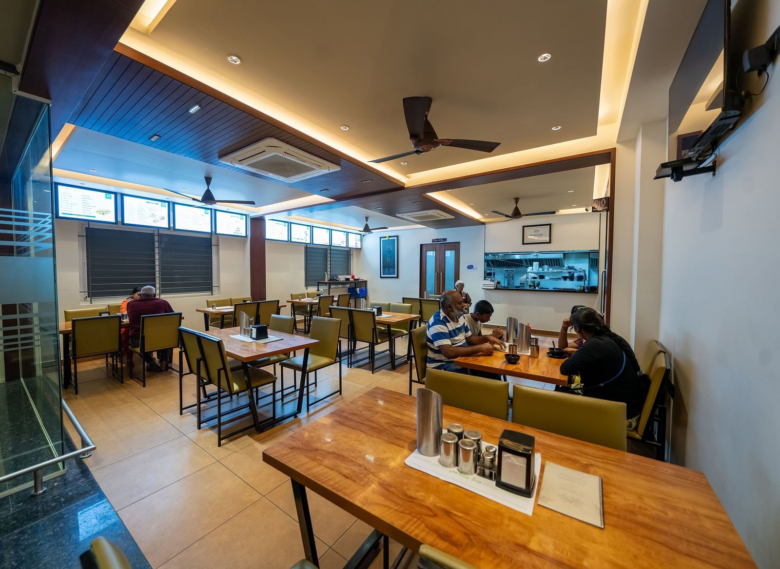 Diagonal view of the dining area at Hari Govinda's, with a neatly arranged table and chairs, and lighting featured in the ceiling corner