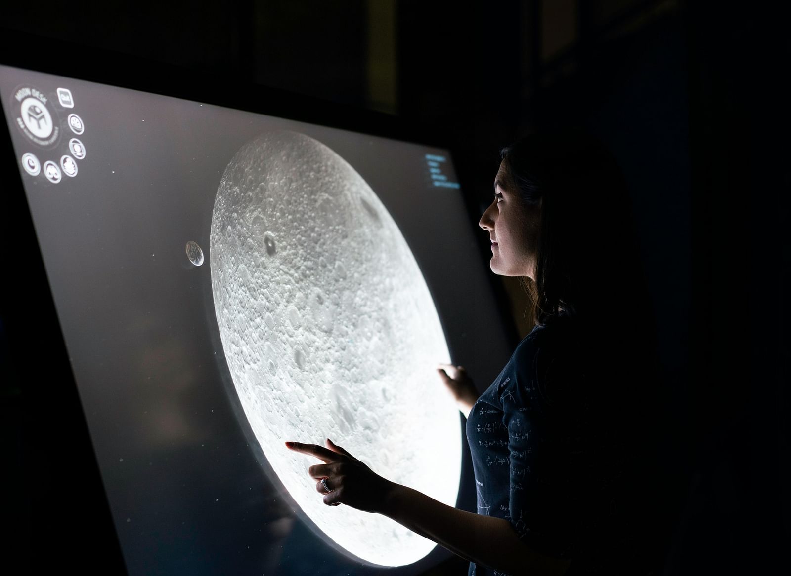 A person looking at and pointing to an illuminated image of the moon.