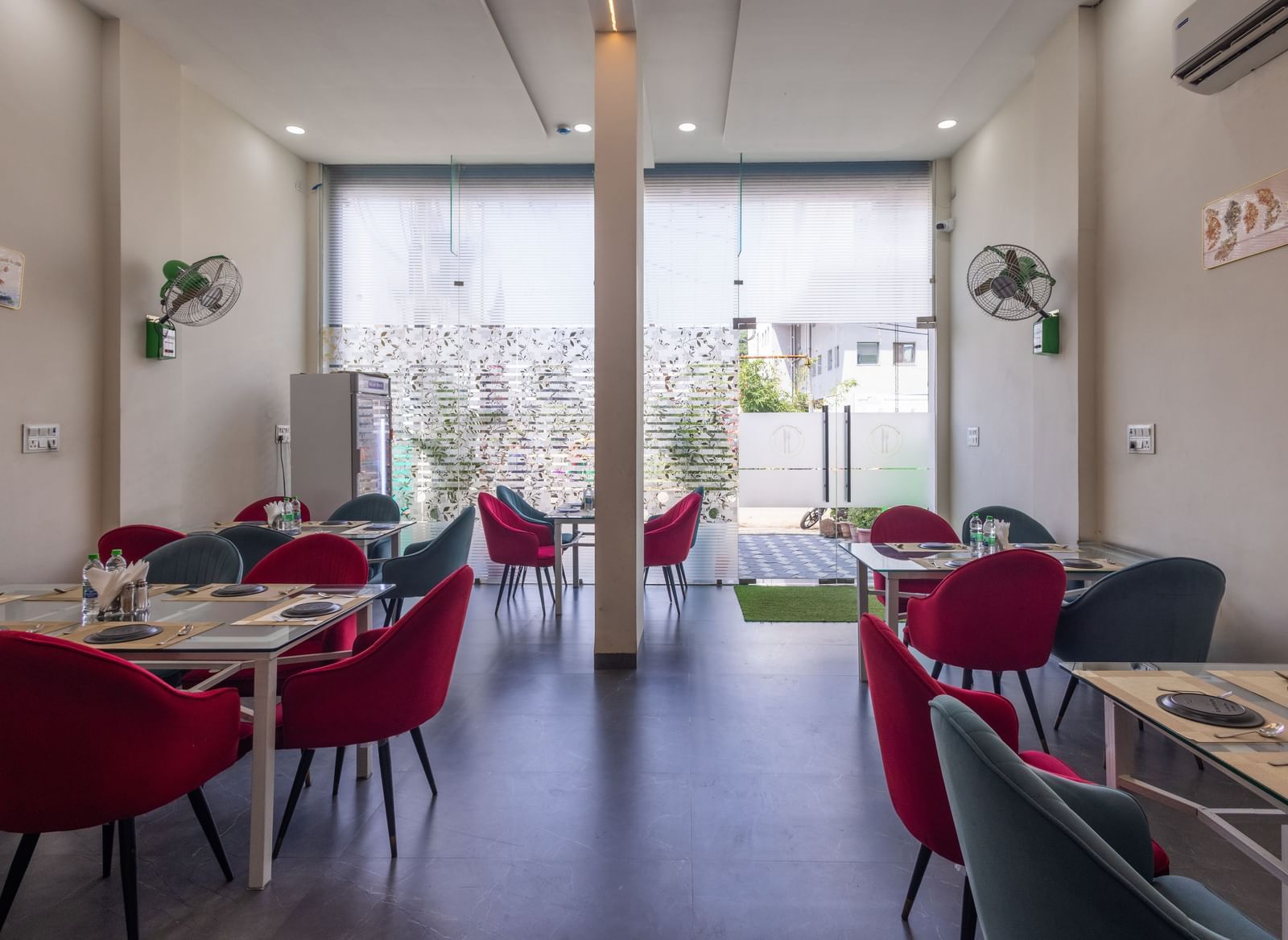 Bright dining hall with glass doors, tables, and red chairs at Pravasa Stay Dewas Naka, Indore.