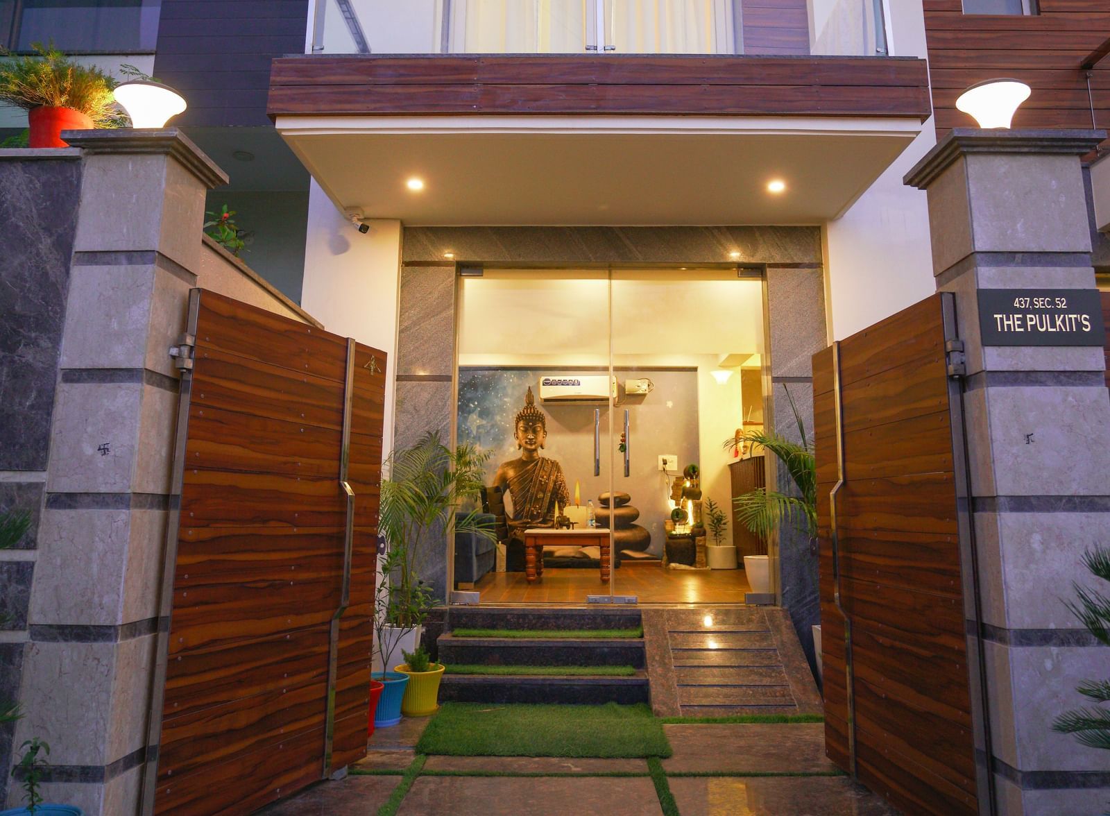 Entrance of Lime Tree Hotel, Pulkit featuring wooden gate, stairs leading to the reception lobby which has a statue of Lord Buddha. There's also a sitting area with sofa and centre table.