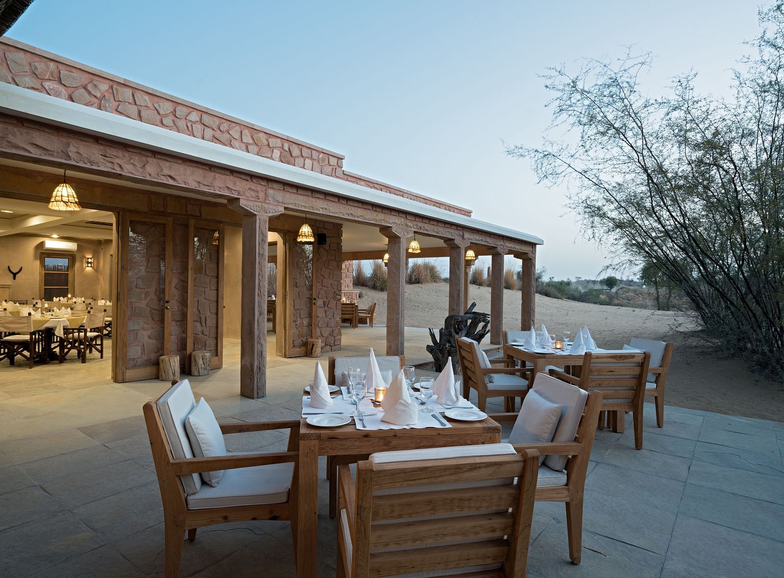 An image of the outdoor dining area set amidst greenery with the sunset view as the backdrop - MANVAR Resort & Desert Camp