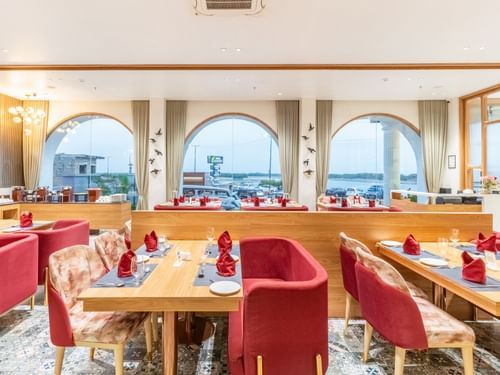 Restaurant at Pride Elite Dwarka featuring several sets of sofa chairs, chairs paired with a table which has plates, cutlery, glass, and towel.