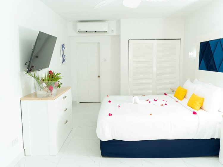 Wide view of the room featuring a king size bed adorned with red flower, facing the T.V., yellow pillows,a wardrobe and a wooden cupboard at The Soco House.