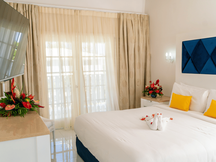 King size decorated bedroom with yellow pillows, facing the T.V. at The Soco House featuring light curtains, headboard and flower bouquets.