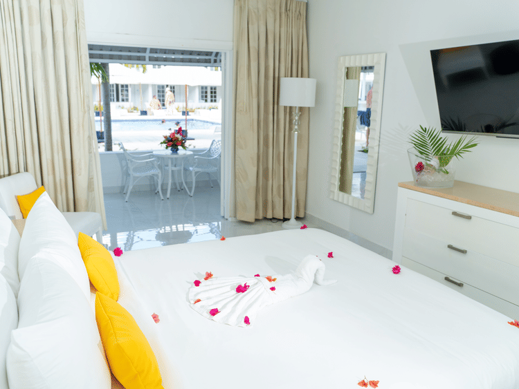 A king size bed with yellow pillows and scattered petals beside a full window at The Soco House.