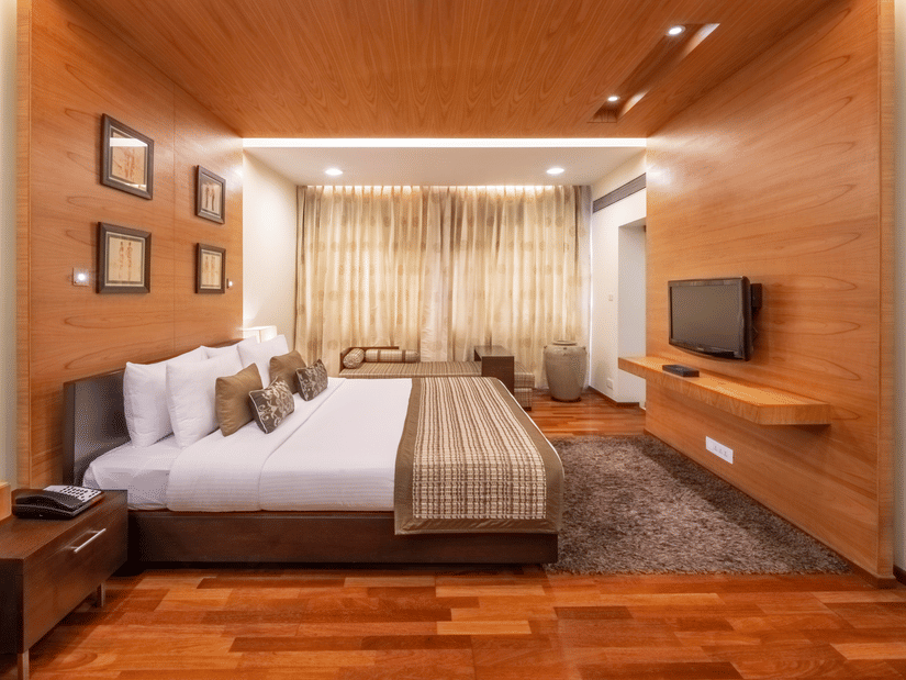 King size bed in the Russel Suite facing the wall-mounted TV and wooden furnishing at Kenilworth Hotel, Kolkata under warm lighting