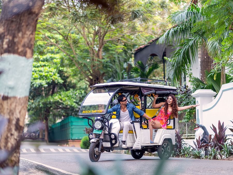 Colourful tuk-tuk parked under lush trees at a tropical resort entrance.