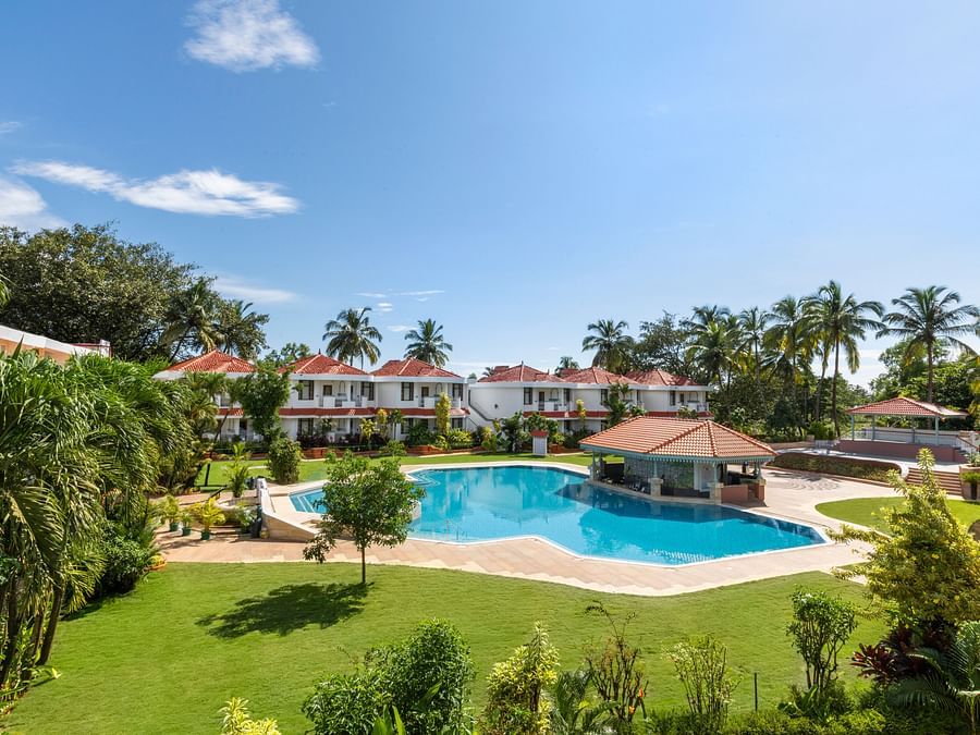 A view of the Poolside Lawn with a swimming pool, a spacious green garden, and large trees surrounding the area - Heritage Village Resorts & Spa