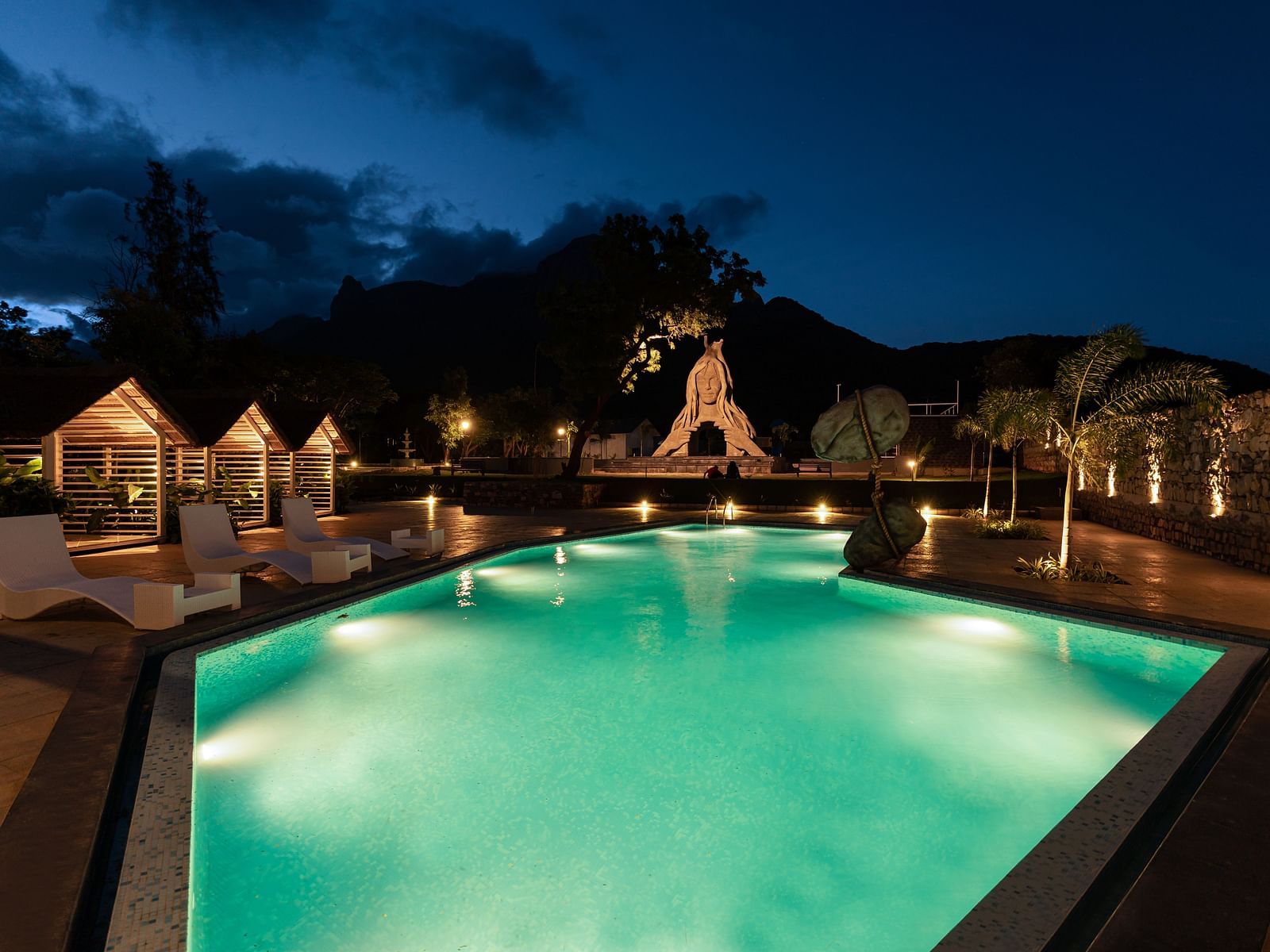 image featuring the expansive swimming pool in the night with a stone statue in the background - Darza Resorts