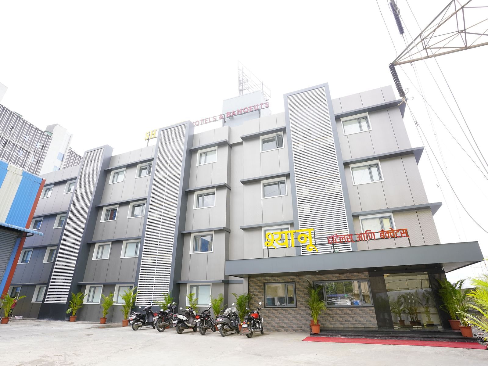 A wide exterior view of the 'Shyanu Lords Eco Inn Hotel' featuring parked motorbikes and potted plants.