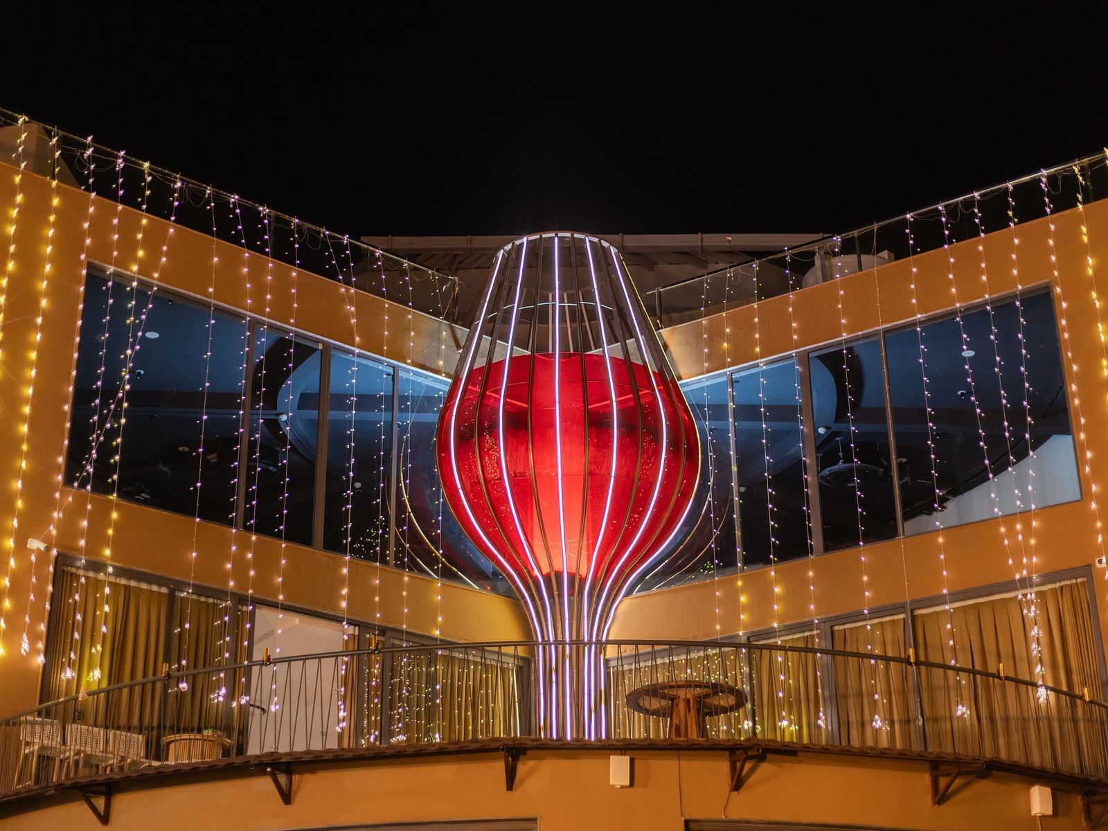 A large red heart-shaped glass decoration hangs in a modern building at night for a wedding | The Qualia Resort Club & Brewery, Udaipur