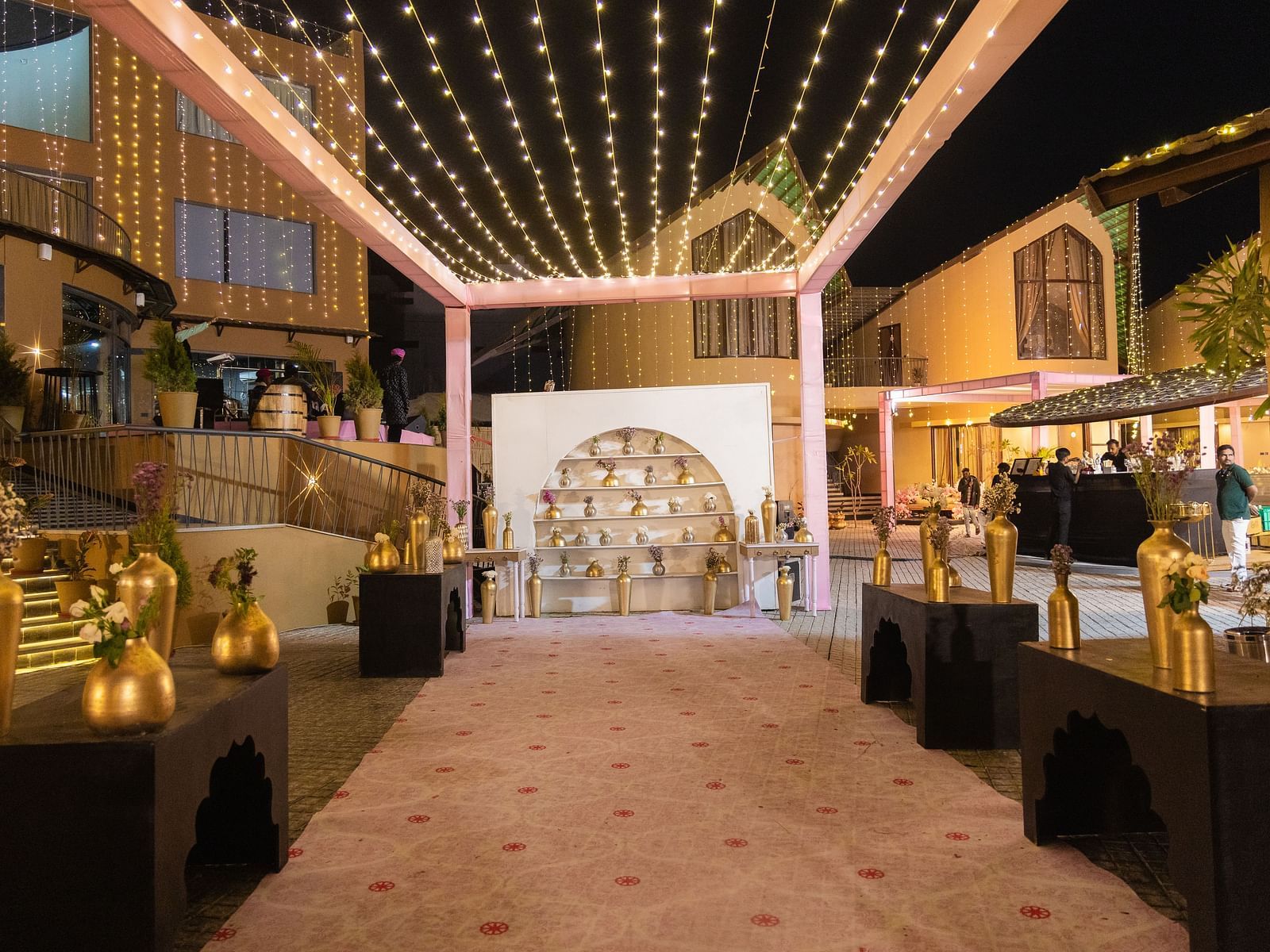 An indoor wedding reception area is decorated with lights, flowers, and tables with food | The Qualia Resort Club & Brewery, Udaipur