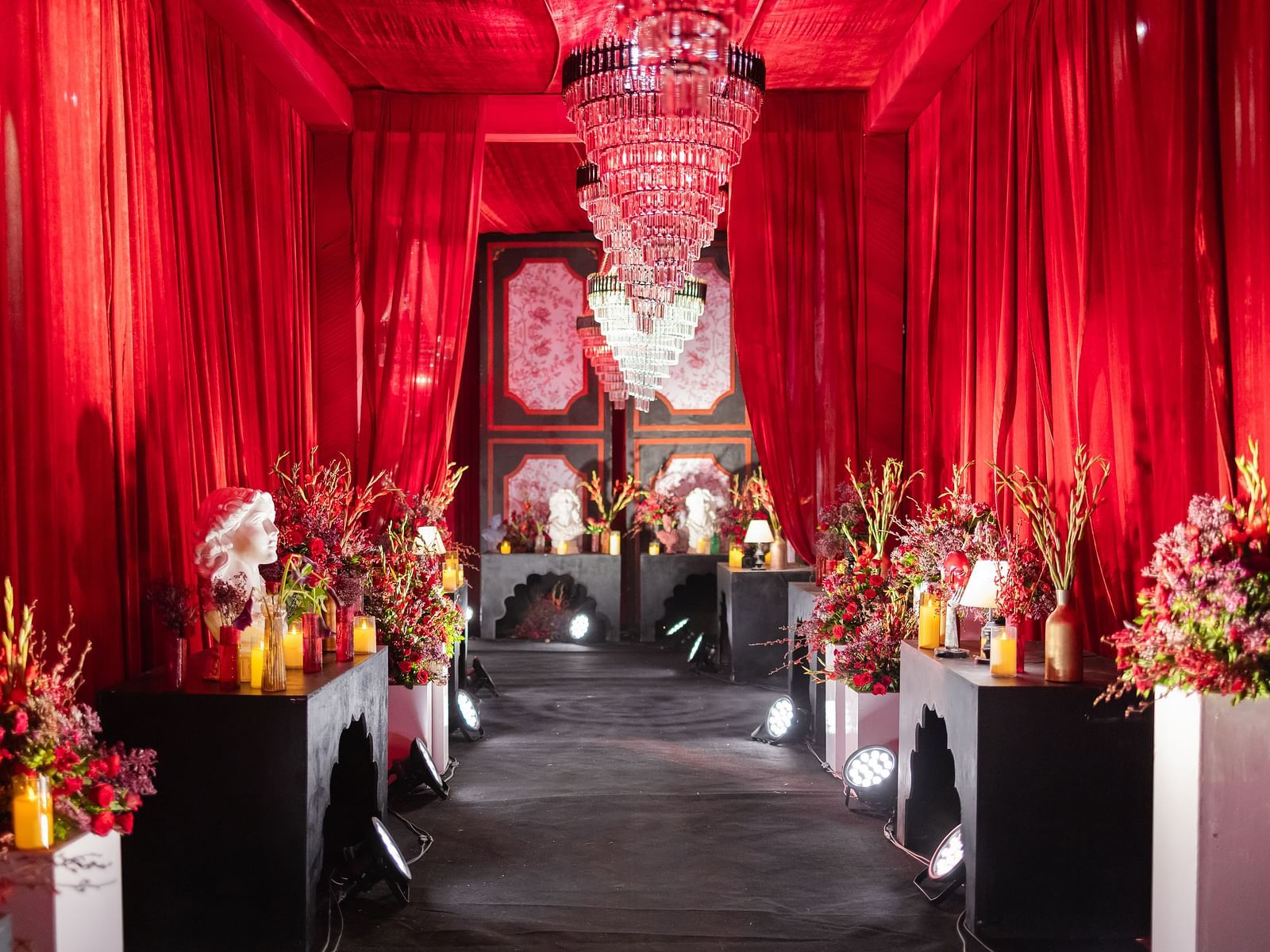 An indoor wedding aisle is adorned with red fabric, flowers, and candles | The Qualia Resort Club & Brewery, Udaipur