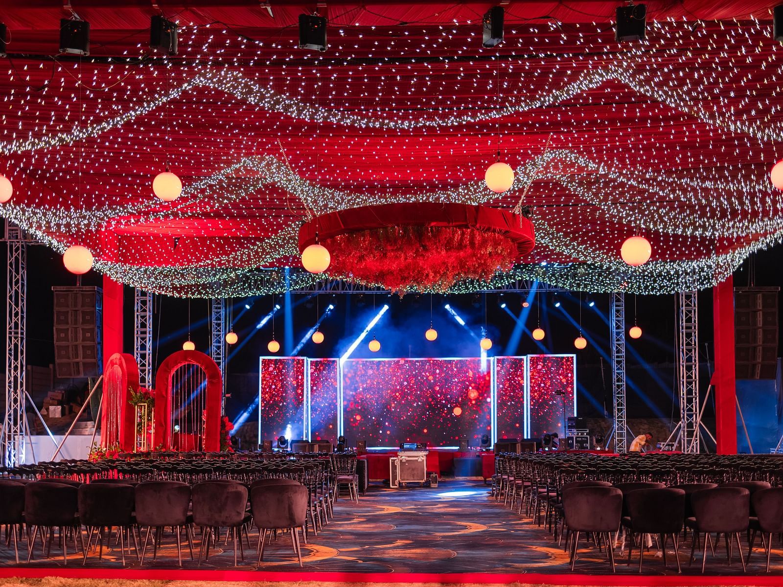 A wedding stage is decorated with red draping and lights indoors | The Qualia Resort Club & Brewery, Udaipur