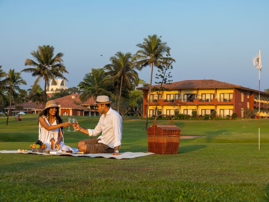 a couple on a picnic in the garden with a building in the background - Caravela Beach Resort Goa