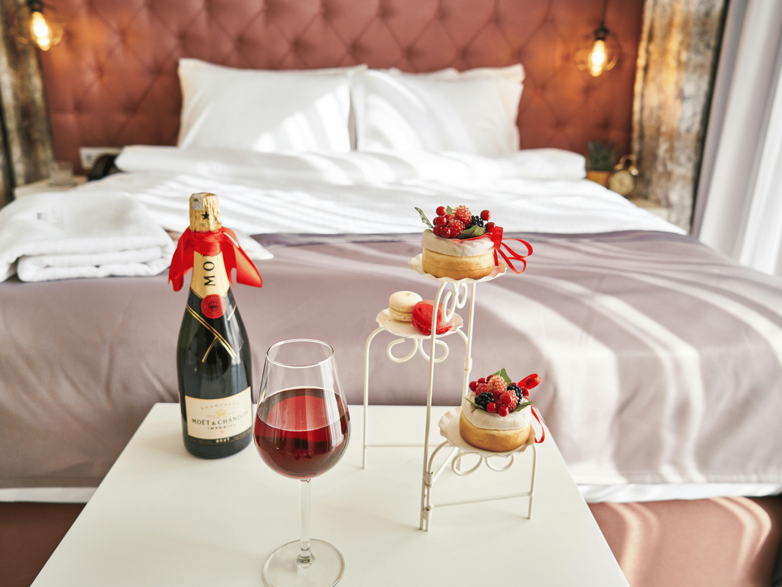 Elegant room setup, Indore with wine, champagne, and desserts arranged beside a bed for a romantic stay.