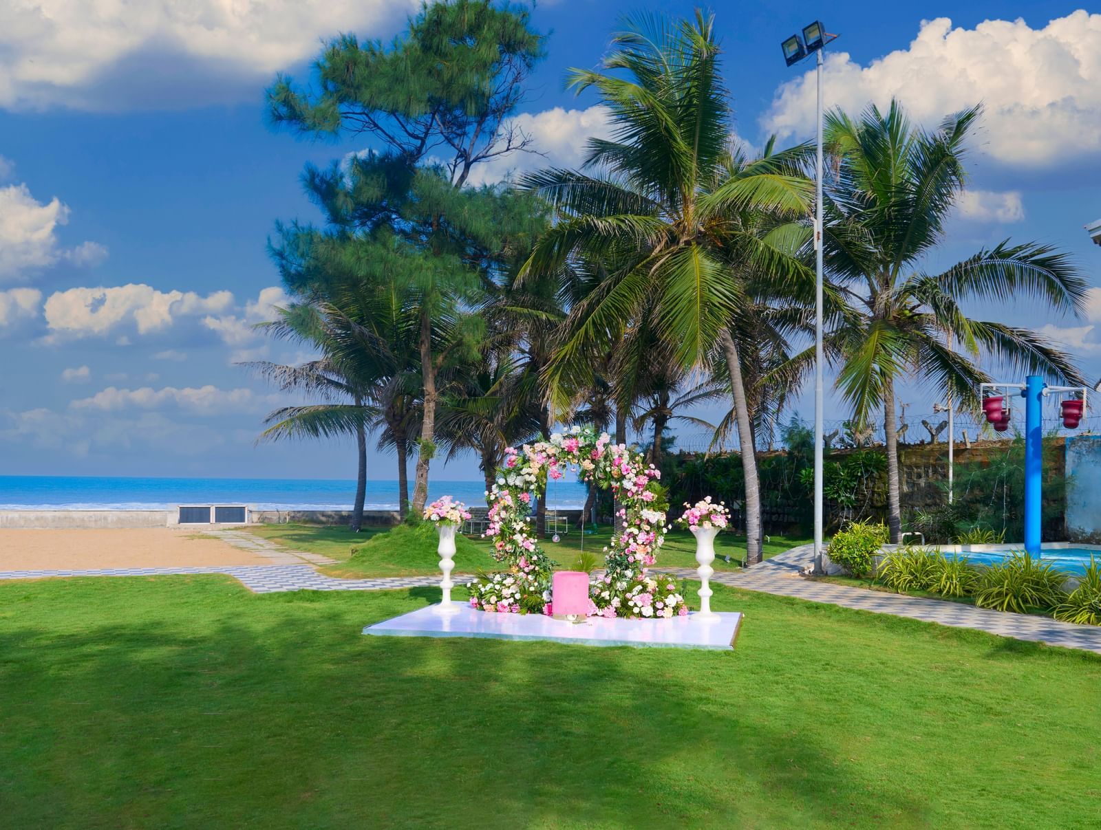 An outdoor decorated space with green trees at the back and the sea & partly clouded sky visible at the backdrop at Grande Bay Resort & Spa.