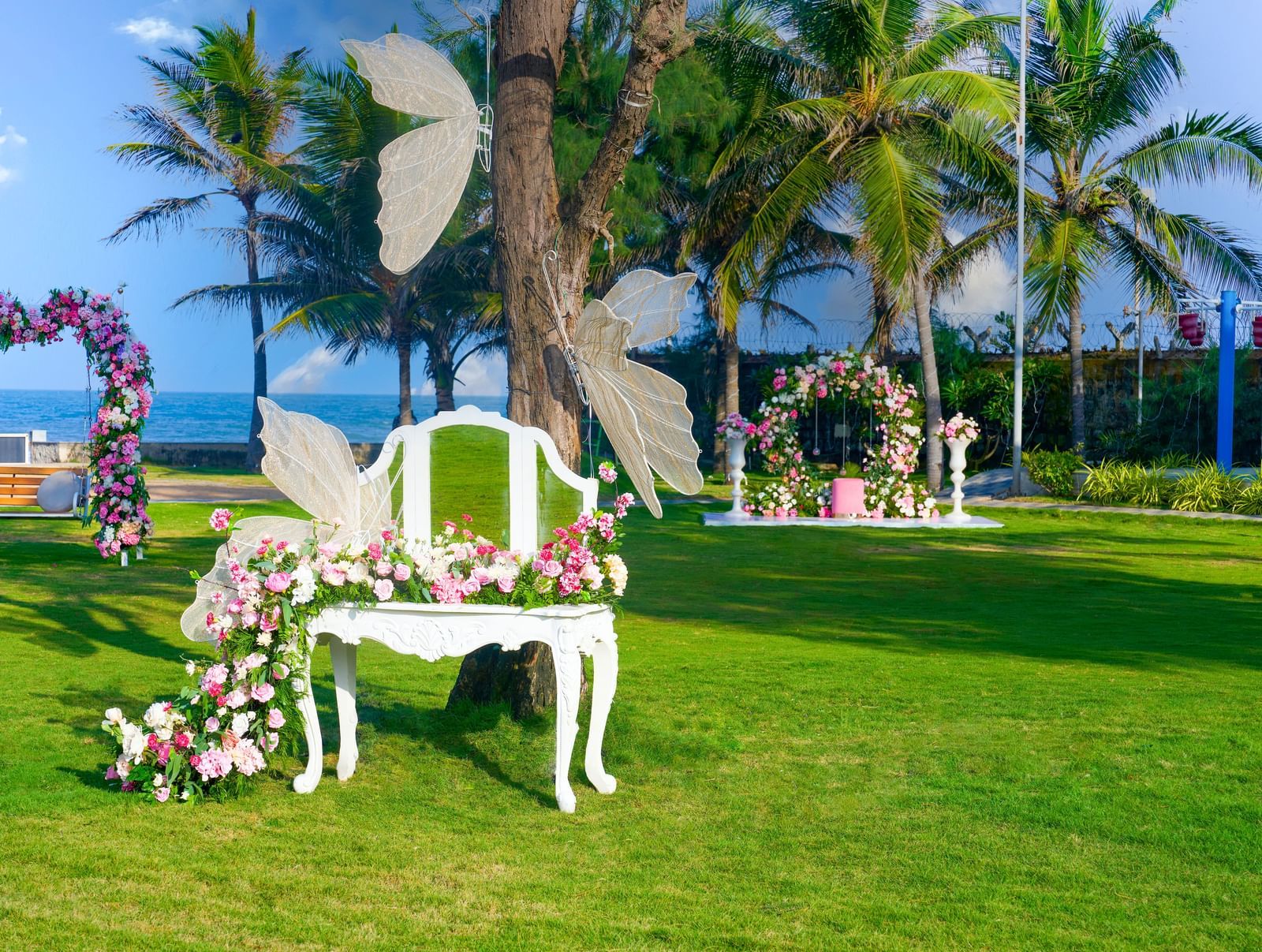 A flowery decorated chair in an outdoor lawn with artificial butterflies attached to the chair and the tree with greenery at the backdrop at Grande Bay Resort & Spa.