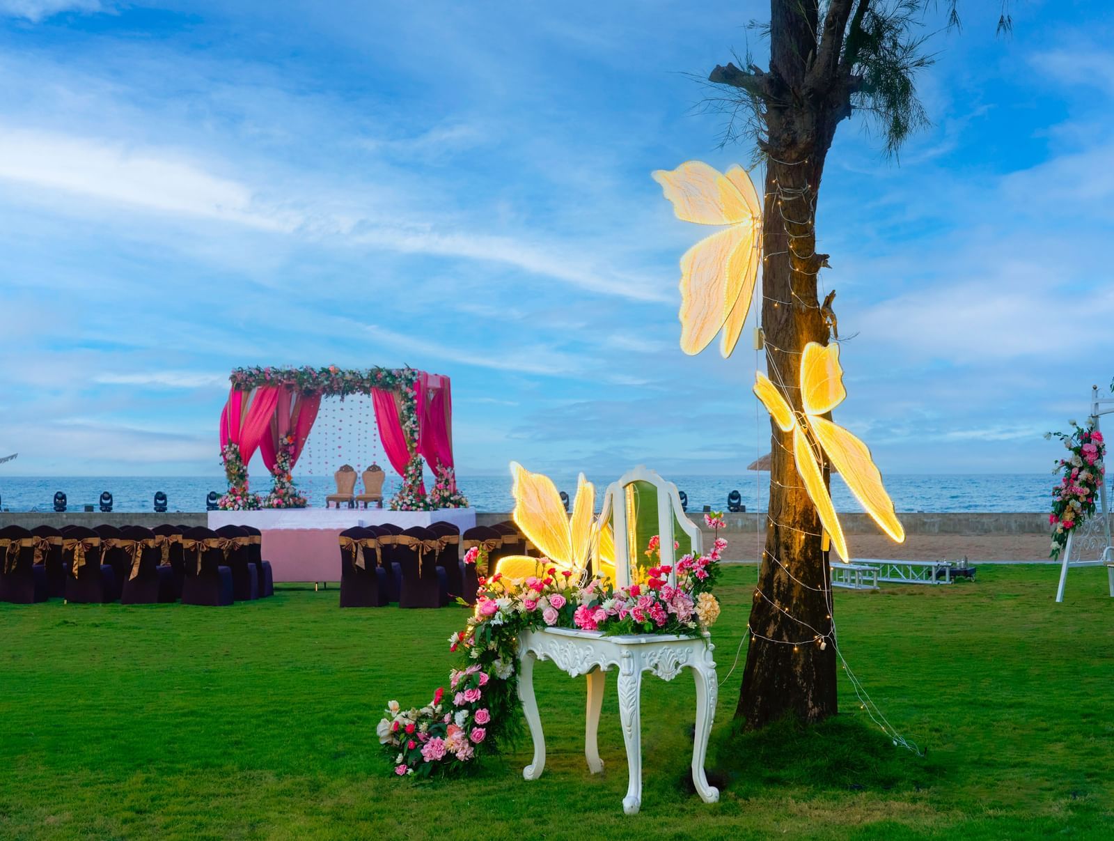 A view of the lawn with a decorated chair and a tree with chairs & a stage visible at the backdrop at Grande Bay Resort & Spa.