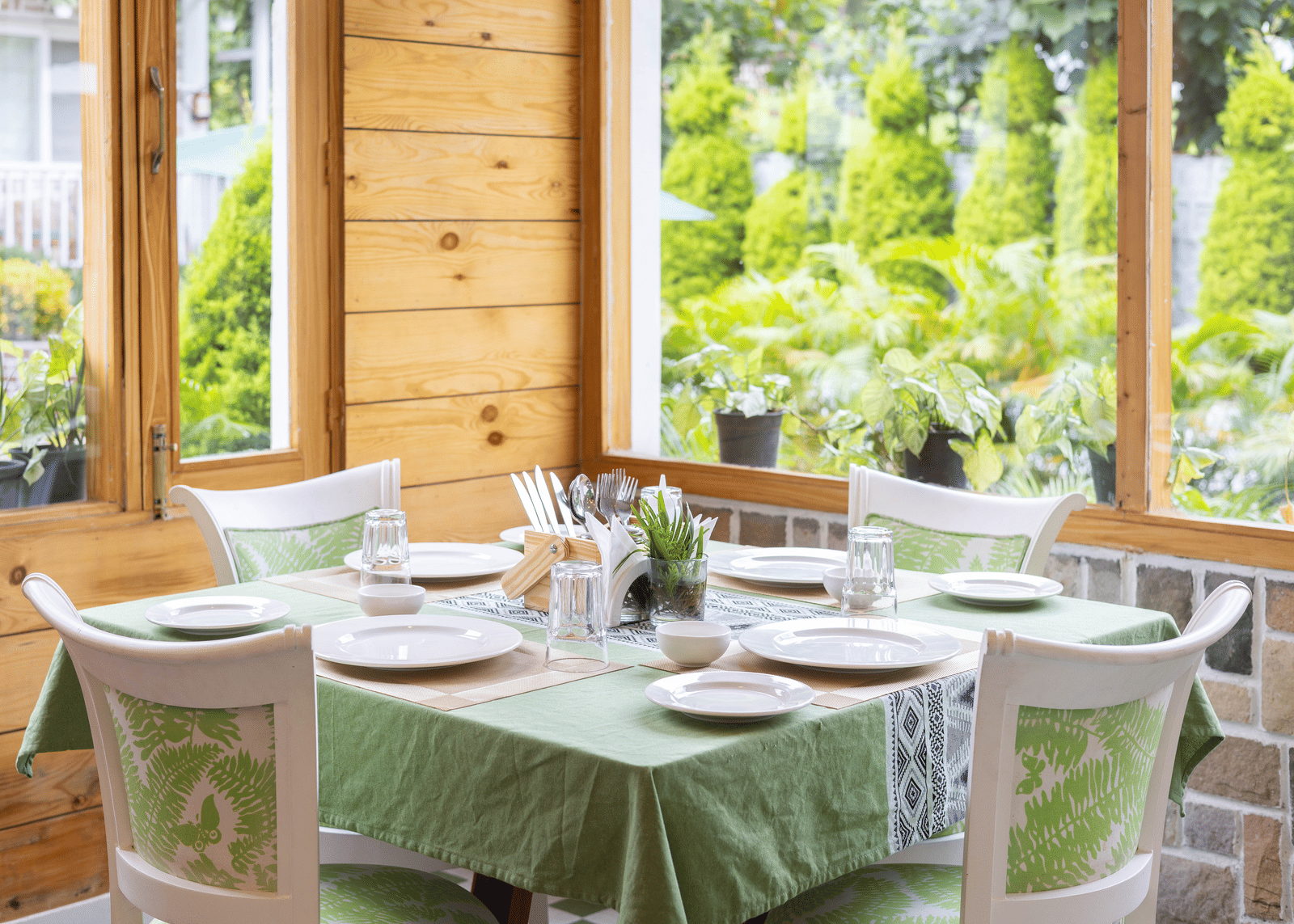A restaurant dining area featuring wooden walls, large windows, and a set table covered in a green cloth - Megha Resort & Villas, Dehradun