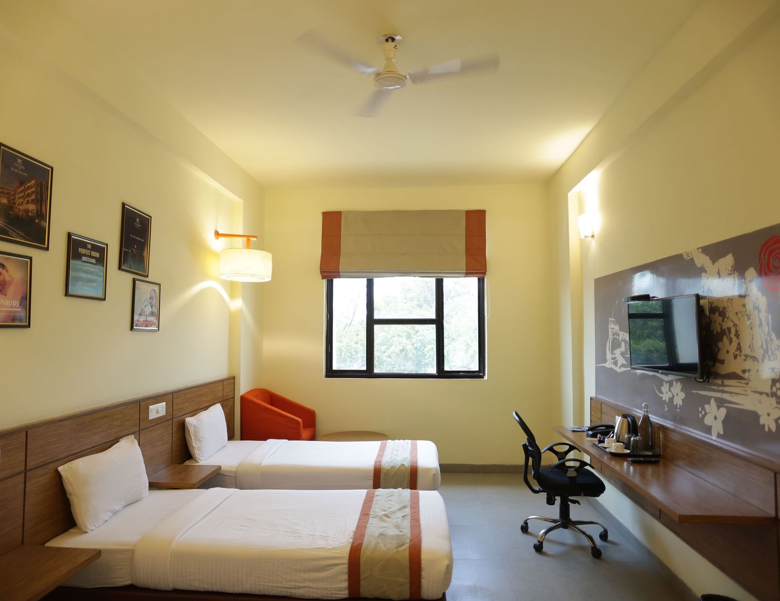 full view image of a room featuring the single beds placed opposite the television along with a window and a cushioned armchair in the far end - Max Hotel Jabalpur