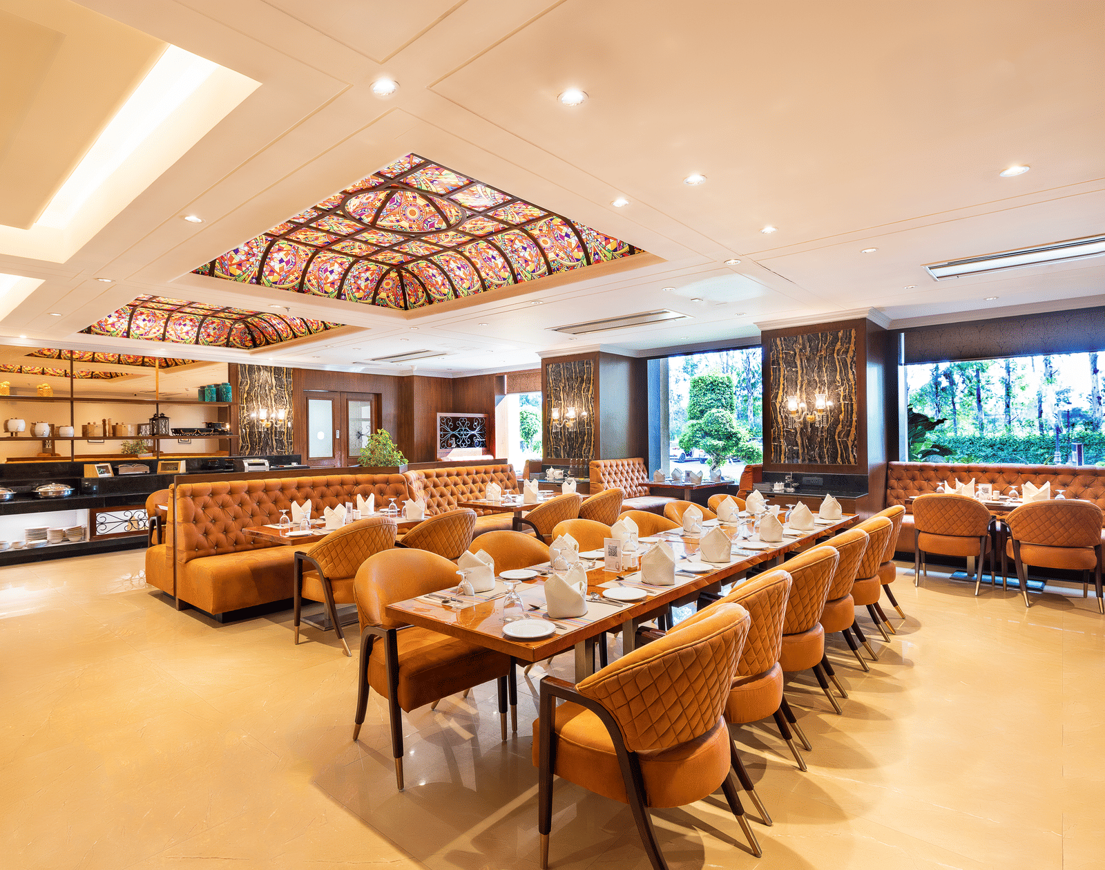 Long view of the spacious restaurant with multiple dining tables, comfortable seating, and a view of the outside through windows at Hotel Hukam's Lalit Mahal.