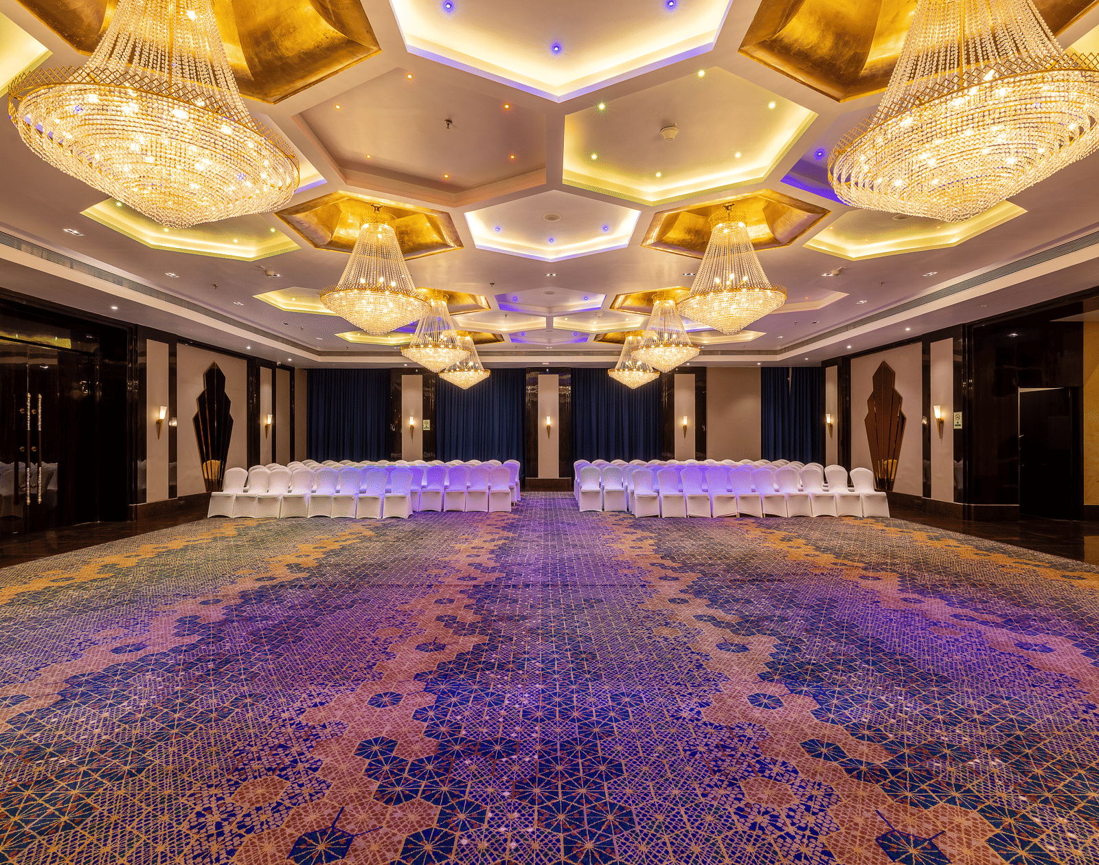 Symmetric view of the large hall featuring multiple tables and chairs, dominated by the elaborate honeycomb chandeliers at Hotel Hukam's Lalit Mahal.