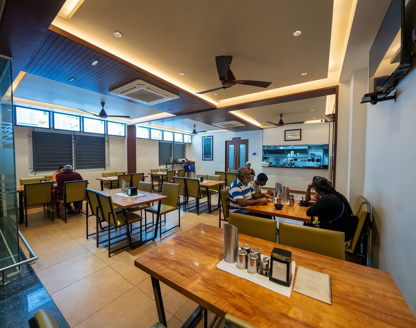 Diagonal view of the dining area at Hari Govinda's, with a neatly arranged table and chairs, and lighting featured in the ceiling corner