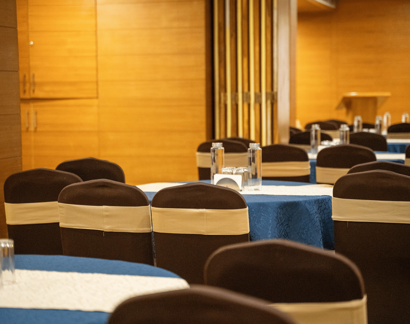 A banquet hall with round tables covered in blue tablecloths and brown chairs - Hotel Udai Median, Udaipur.