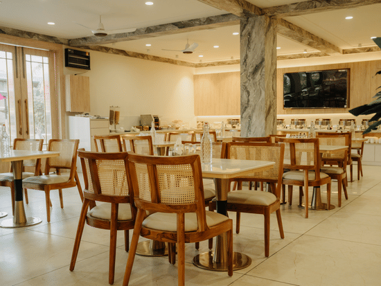 Restaurant interior at Corbett Adventure Resort, Ramnagar showing organised table settings, natural tones, and a central buffet area.