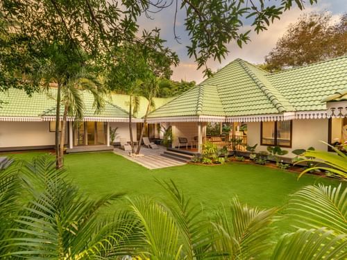 Cottages and villas at Heritage Village Resort and Spa, Goa surrounded by a lawn, some grass and trees.