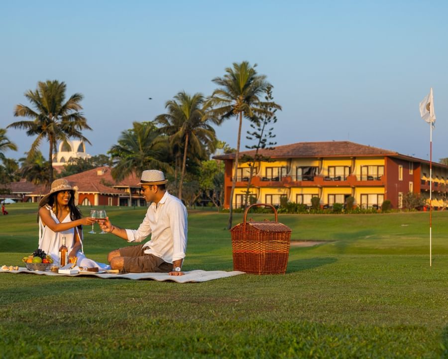 a couple on a picnic in the garden with a building in the background - Caravela Beach Resort Goa
