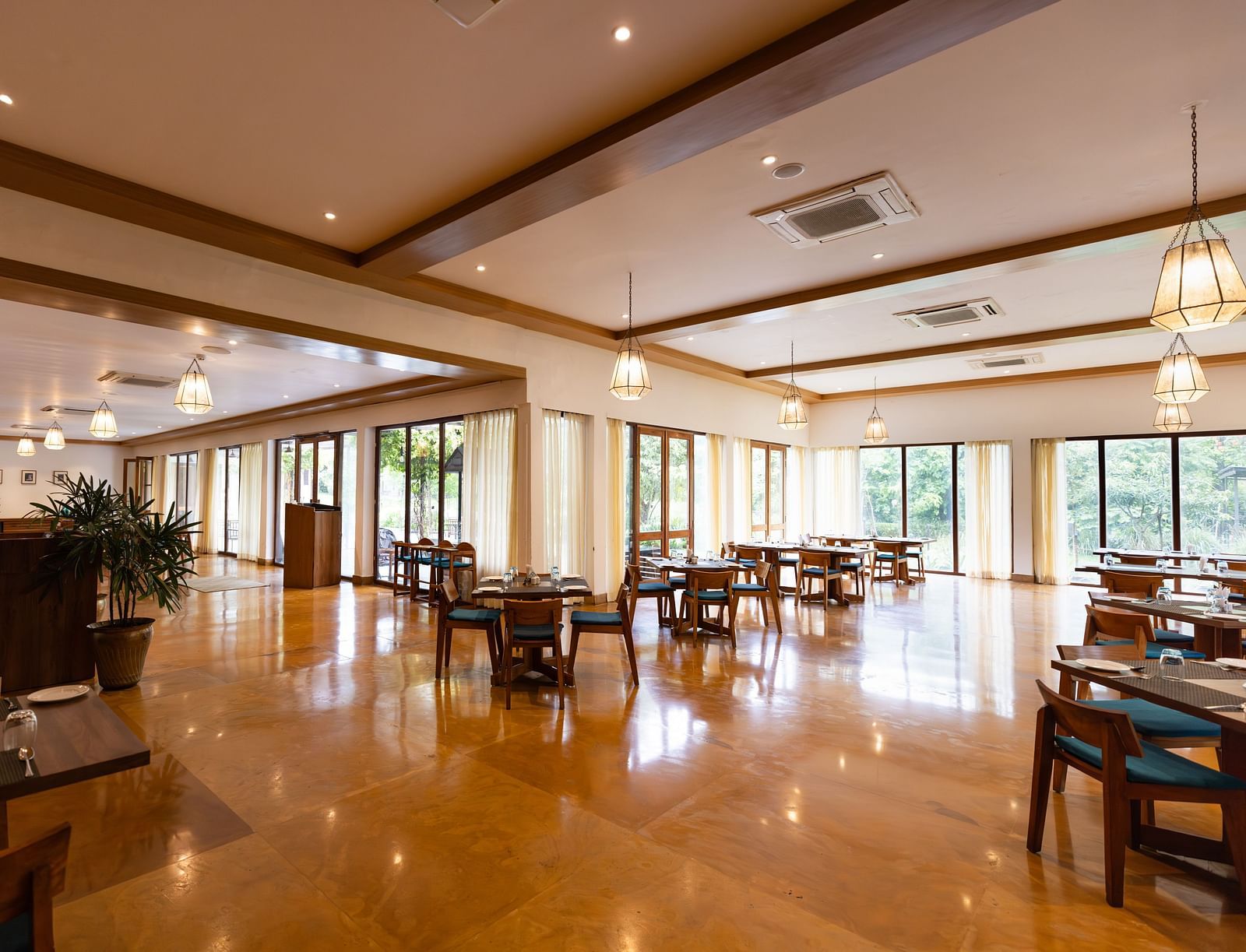 Seating arrangement in Azrak Restaurant at Saraca Resort & Spa Corbett with wooden flooring and wooden panelling on the ceiling alongside large French windows bringing in lots of light