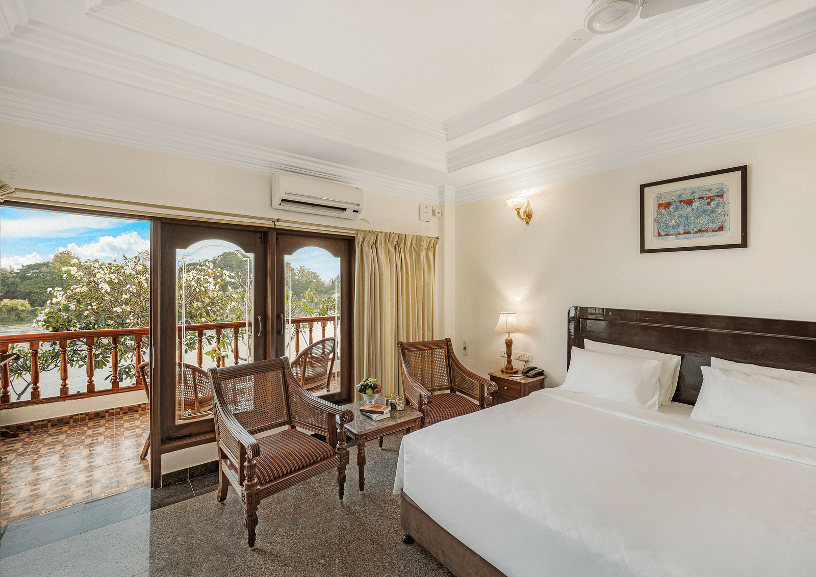 An image of the River Edge Heritage Room featuring a queen size bed, bed side table, lamps, and chairs - GReaT Trails River View Resort Thanjavur By GRT Hotels