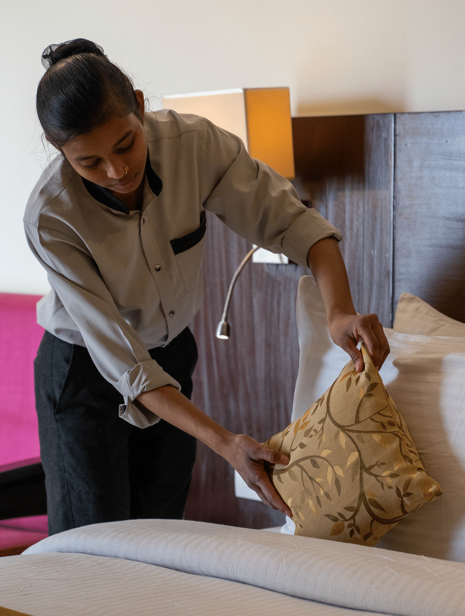 A lady setting up a pillow on a neatly made double bed | Hotel Udai Median, Udaipur