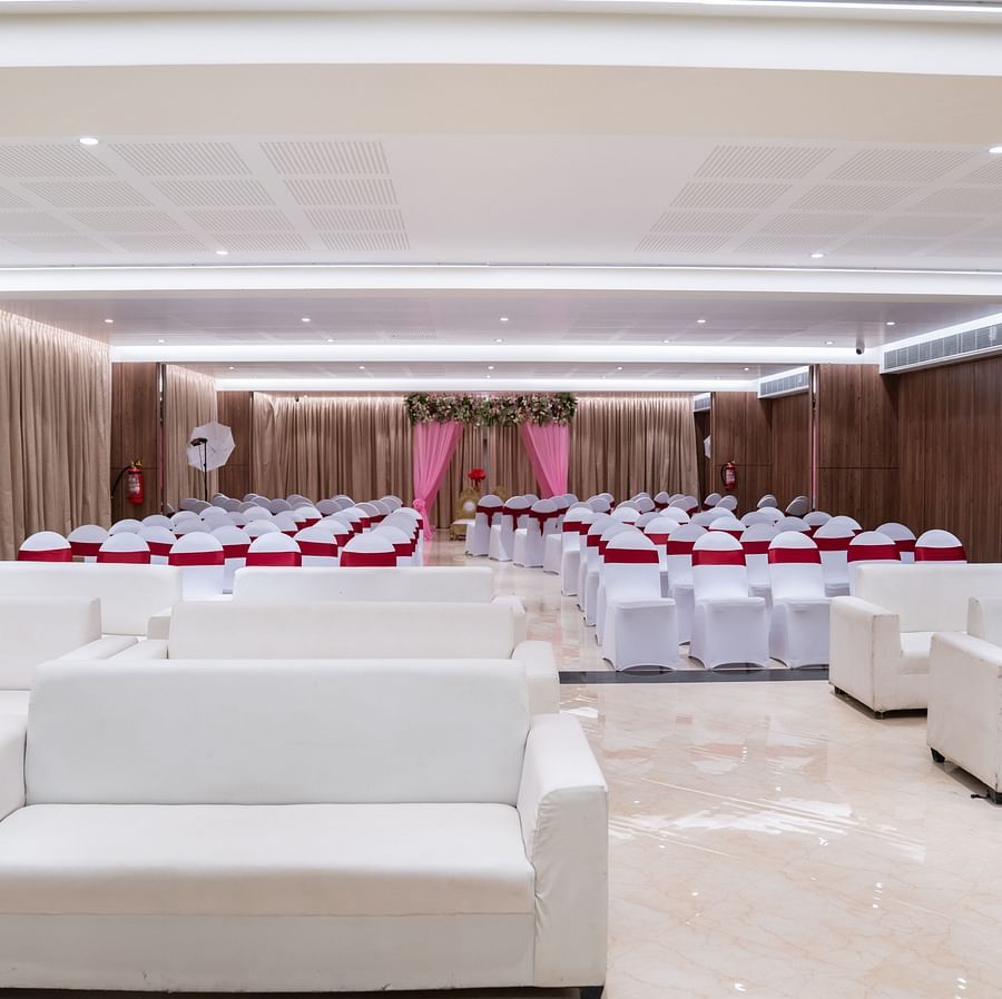  A banquet hall with rows of chairs and a stage, decorated with curtains and floral arrangements.