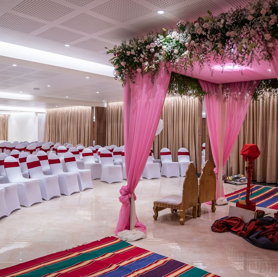 A wedding mandap decorated with drapes, floral arrangements, and a stage with two chairs.