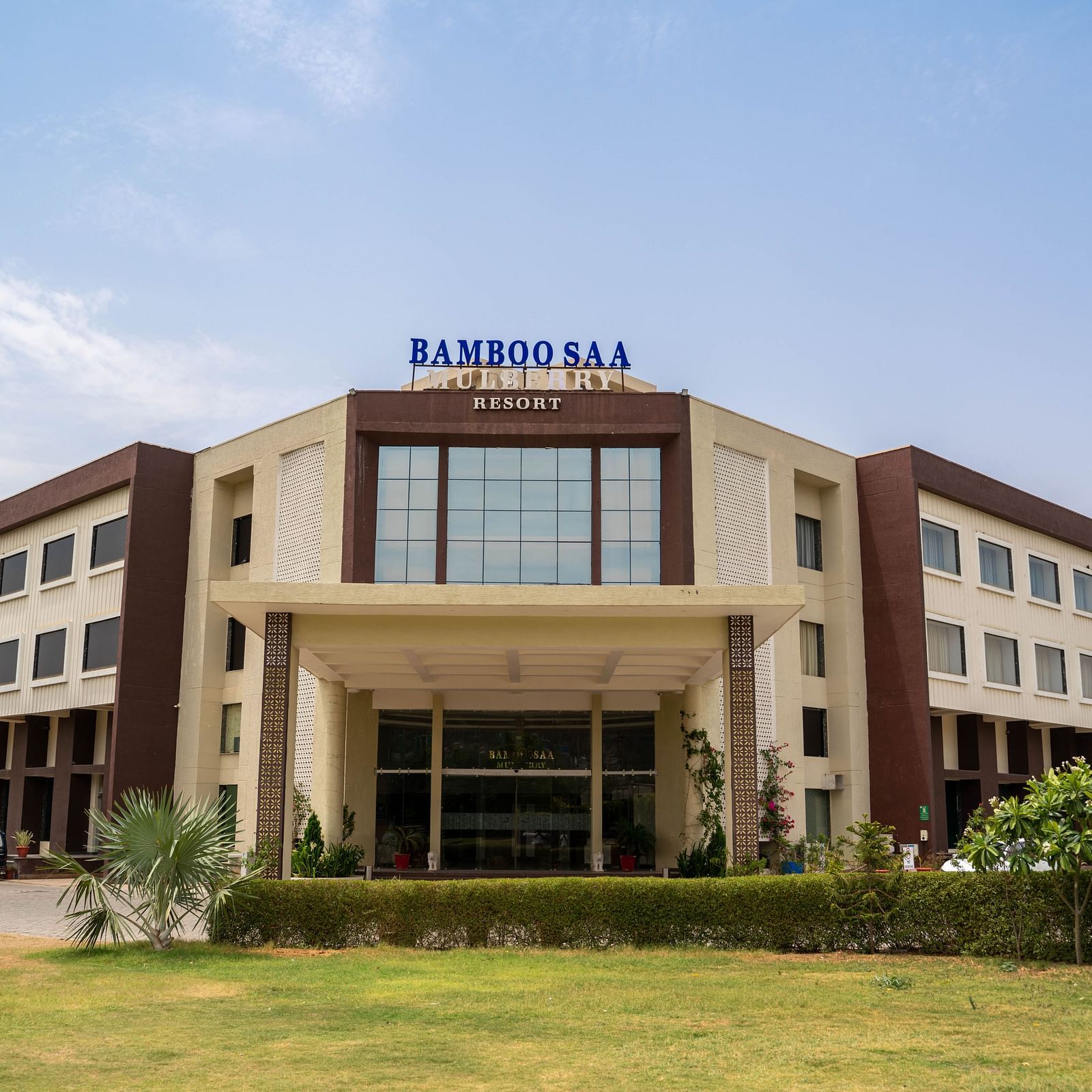 Front view of the grand facade and portico of Bamboo Saa Mulberry Resort, Pushkar with a large logo on a sunny day.