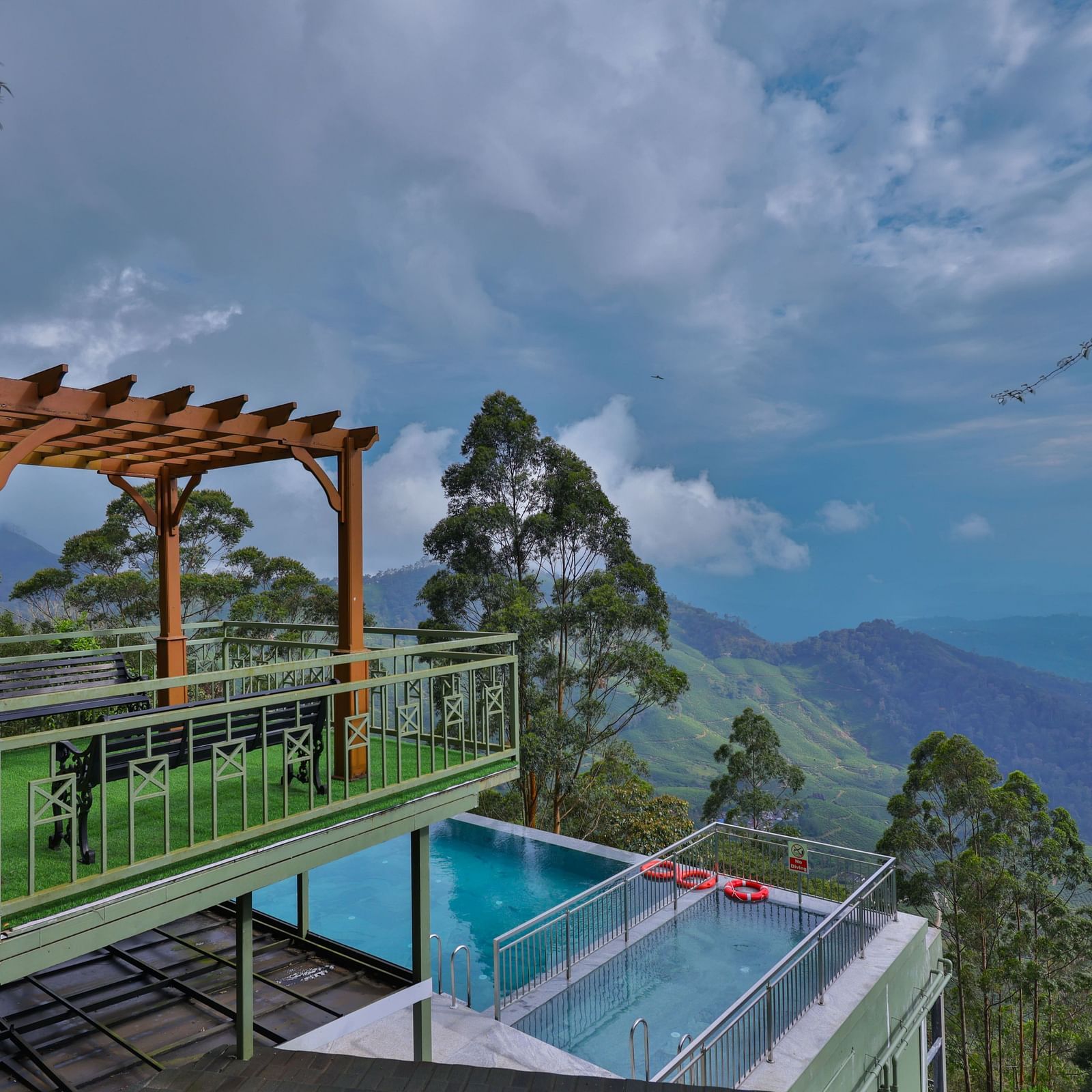 Balcony with a view of the ground-floor swimming pool, surrounded by trees and hills - Fragrant Nature Munnar