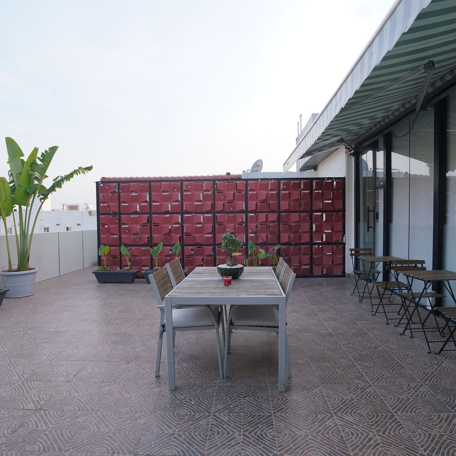 A rooftop dining space with a central table, chairs, and a decorative partition in the background at Kyzen Smart Stays.